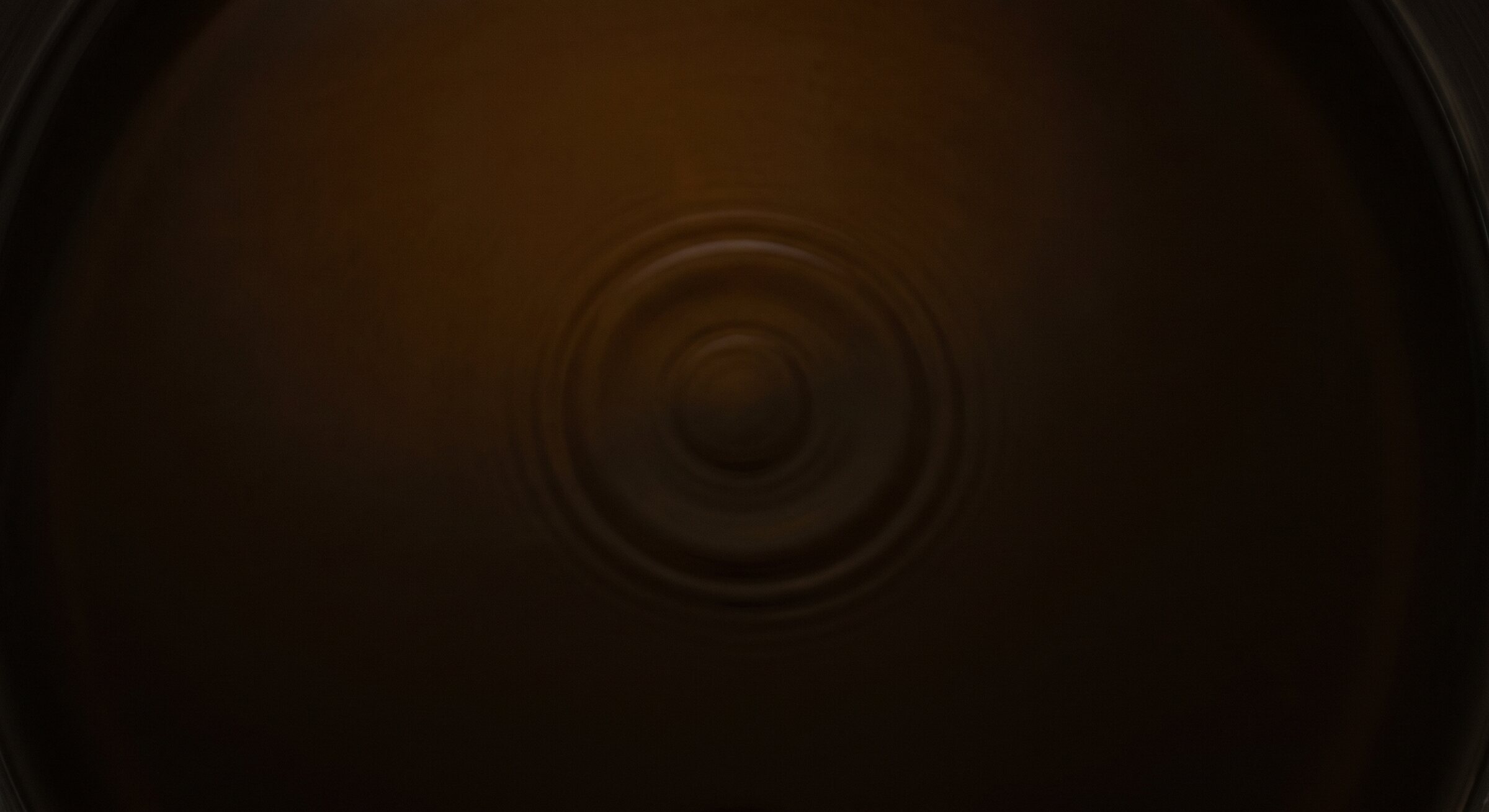The still, dark surface of warm amber oil seen from above, with faint concentric ripples.